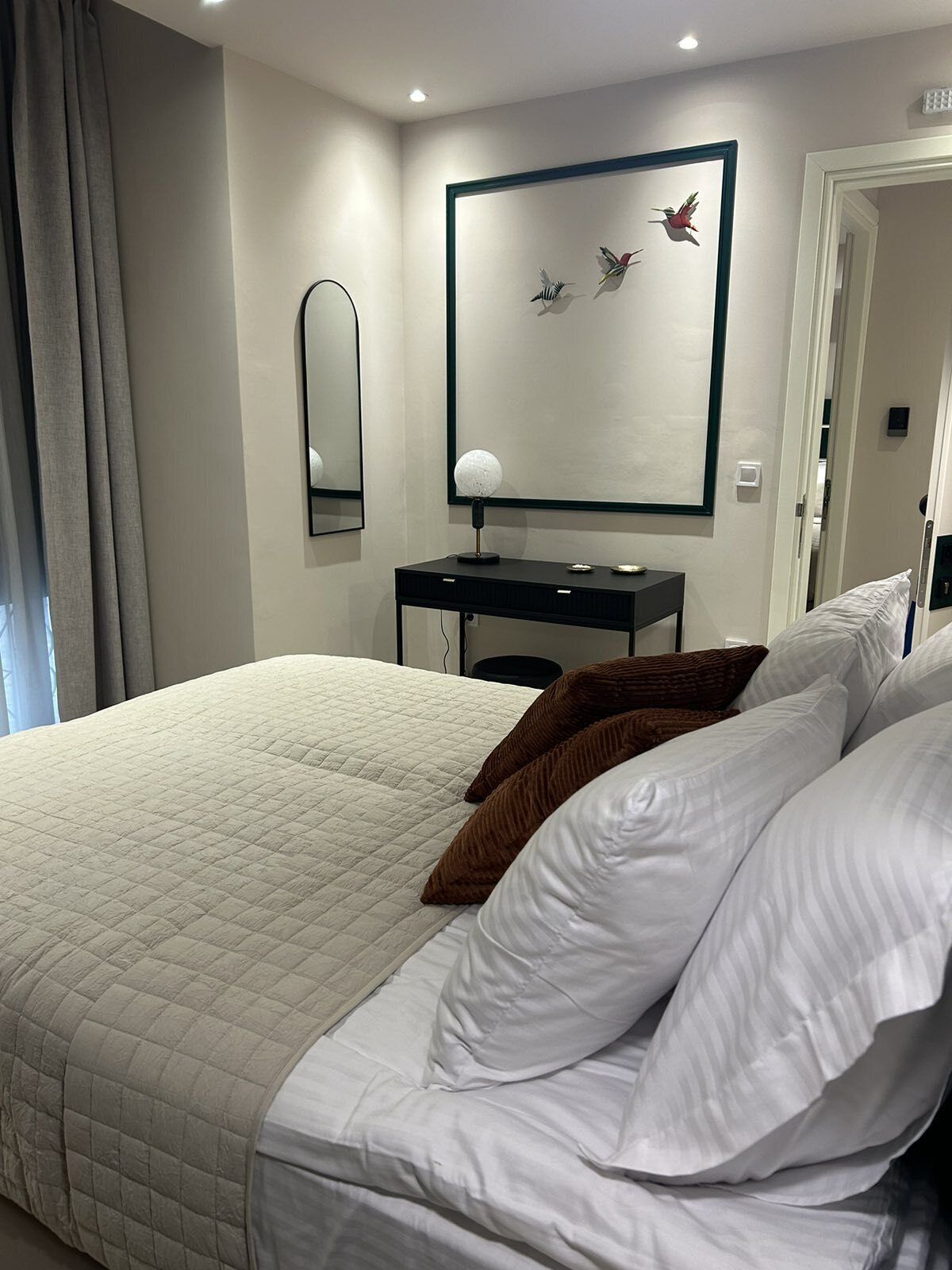 A hotel room with a large bed, a desk, and a mirror.