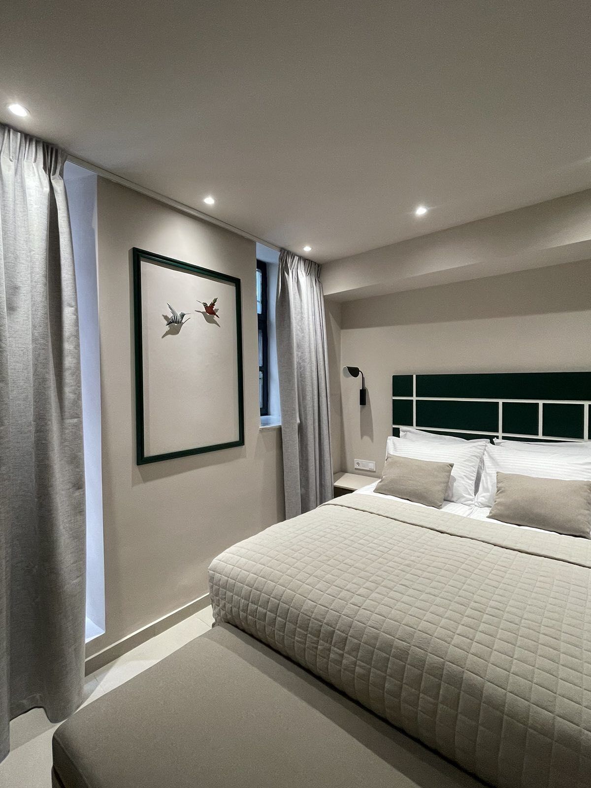 A modern bedroom with a large bed, a headboard, a bedside table, and a wall-mounted lamp.