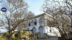A historic building with arched windows and a central entrance, surrounded by leafless trees and a paved street. - Joi Home Beachfront (Ho Chi Minh City)