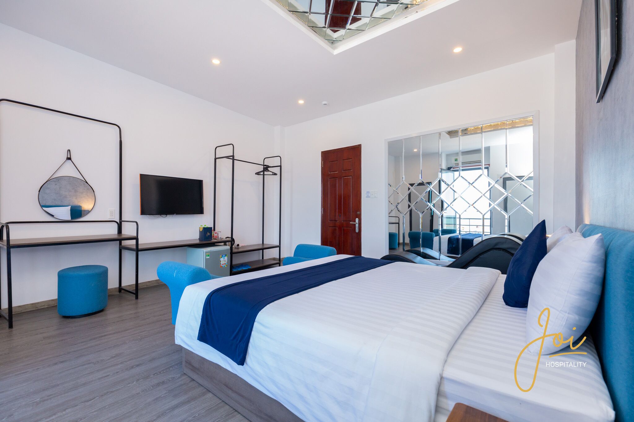 A modern hotel room with a bed, a desk, a chair, a wardrobe, and a TV.