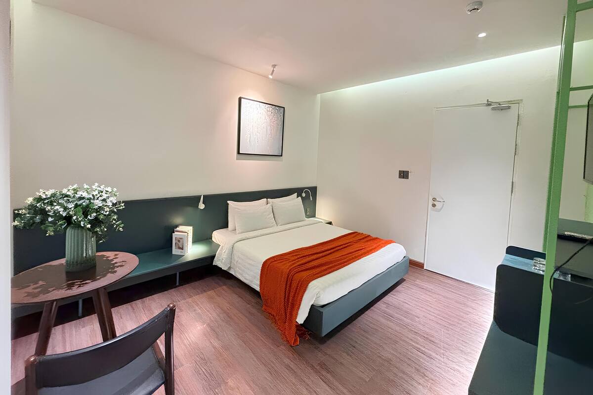 Una habitación de hotel moderna con una cama, una mesita con un florero, una silla y un escritorio con una computadora.