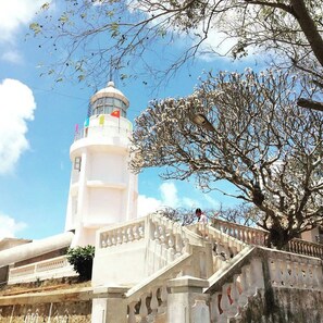 A white lighthouse with a flag, a staircase, and a tree in the foreground. - Joi Home Beachfront (Ho Chi Minh City)