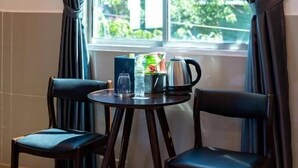 A hotel room with a bed, two chairs, a small table with a kettle, and a window with curtains. - Joi Home Beachfront (Ho Chi Minh City)