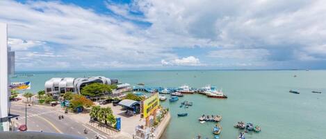 A coastal cityscape with a modern building, a marina with boats, and a clear sky.