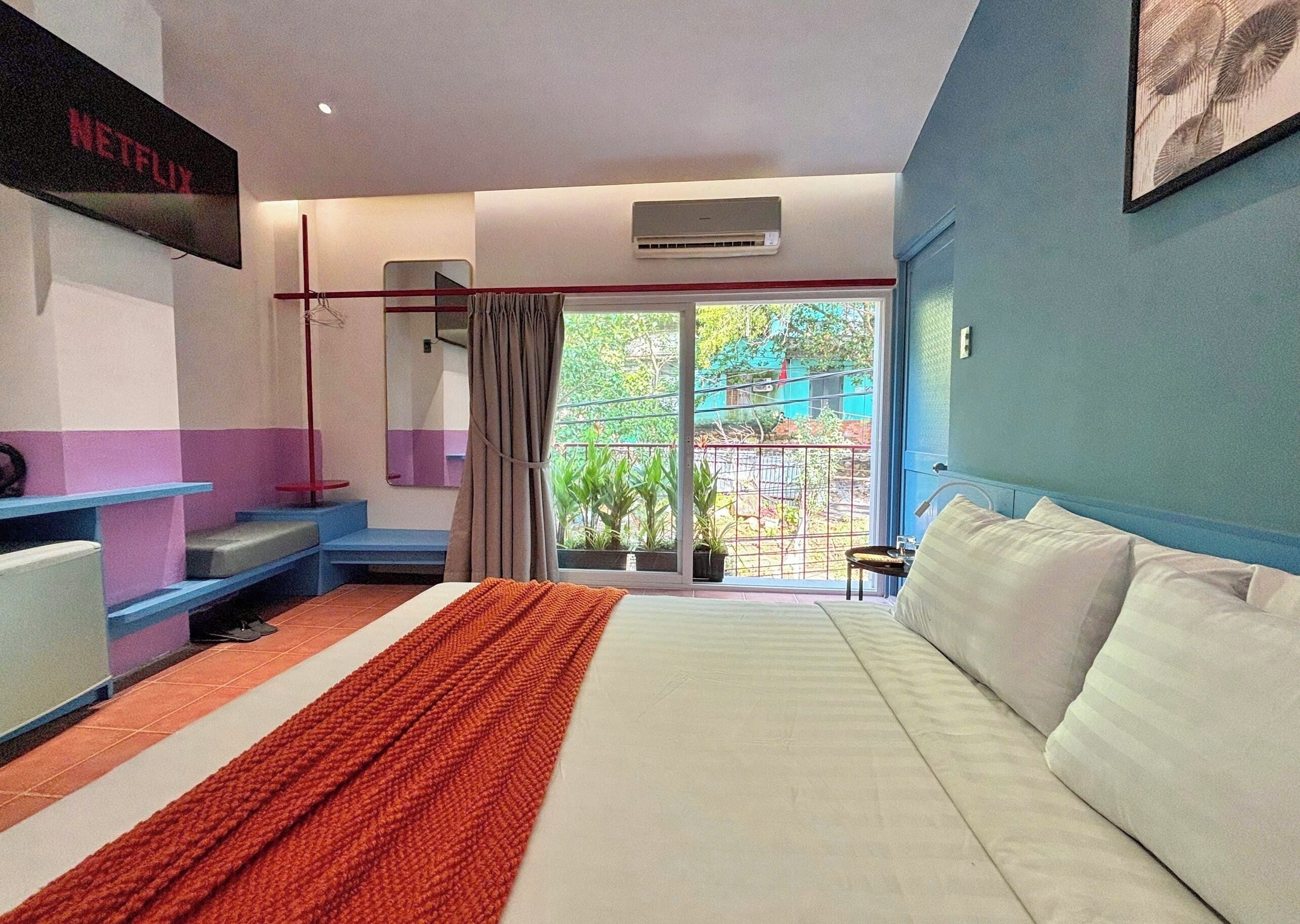Habitación de hotel con cama, televisor montado en la pared, ventana con vista al exterior y balcón.