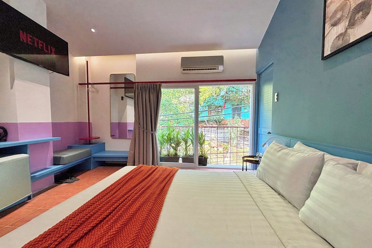 Habitación de hotel con cama, televisor montado en la pared, ventana con vista al exterior y balcón.