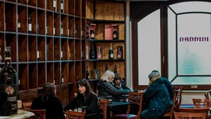 Um restaurante acolhedor com prateleiras de madeira repletas de garrafas, mesas com cadeiras e uma grande janela com o nome "nannini".