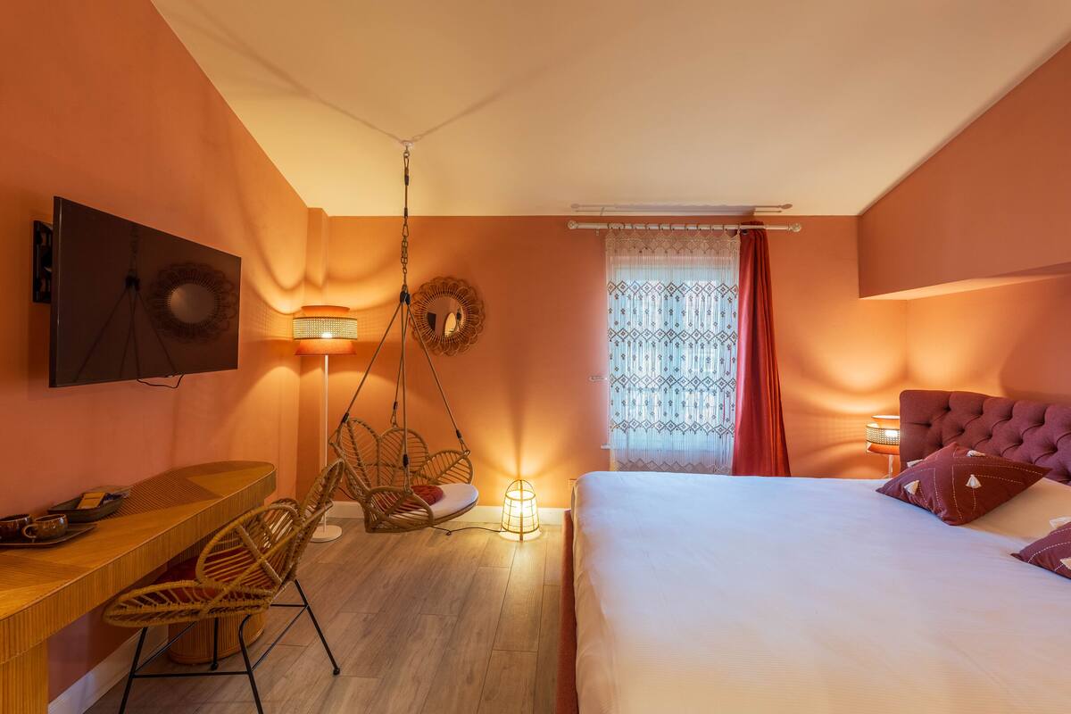 A bedroom with a bed, a desk, a chair, and a hanging light fixture.