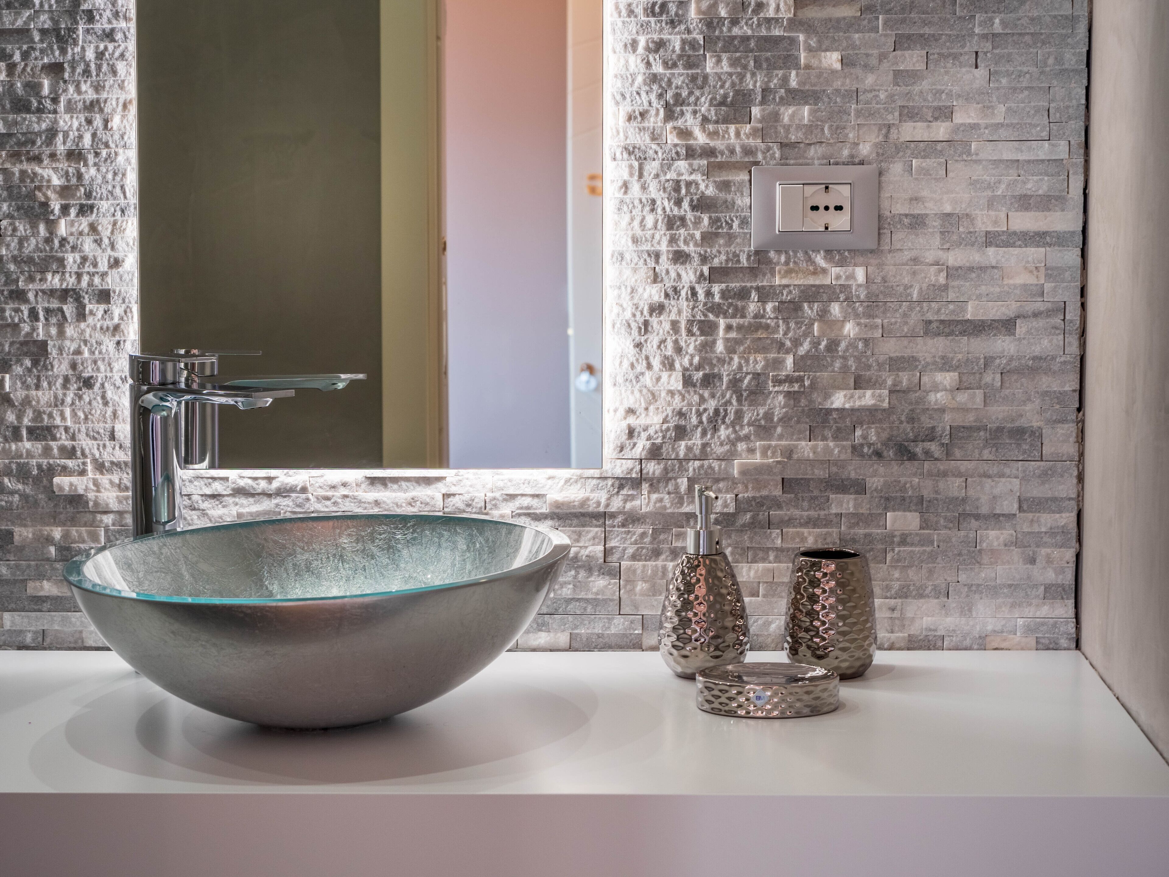 Une salle de bain dotée d’un grand lavabo rond en métal, d’un robinet moderne et d’un mur en pierre à texture.