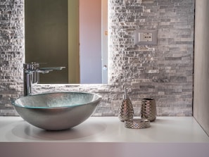 A bathroom with a large, round, metallic basin, a modern faucet, and a textured stone wall. - Blossoms of Siena (Siena)