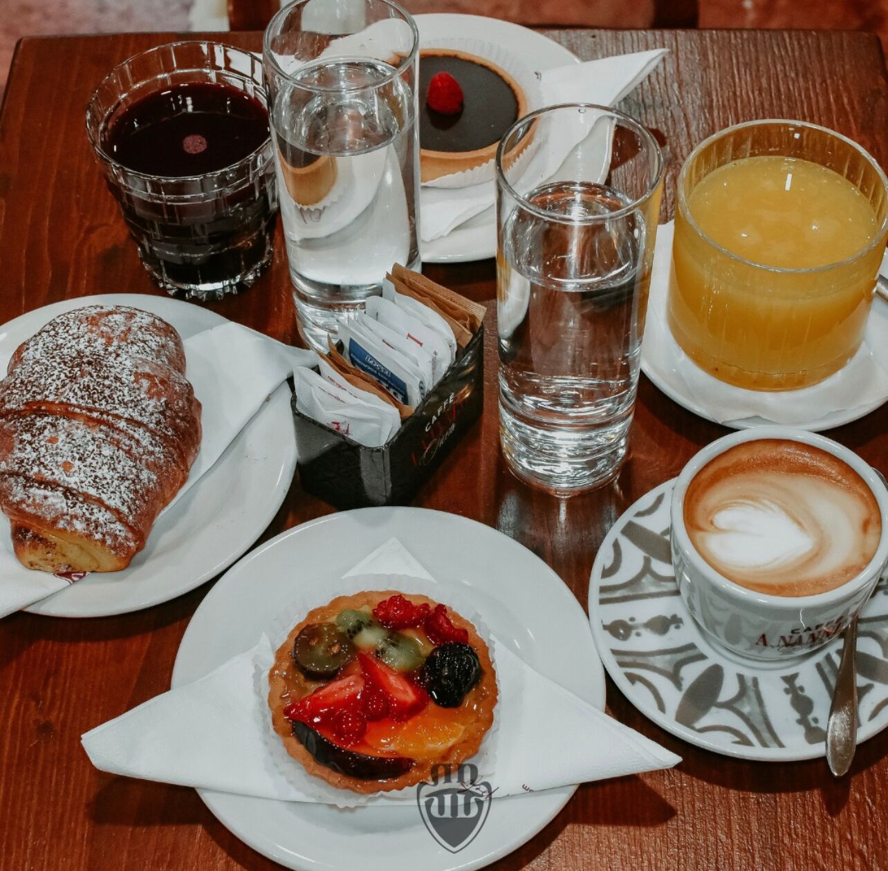 A table with a pastry, a fruit tart, a coffee cup, and various beverages.