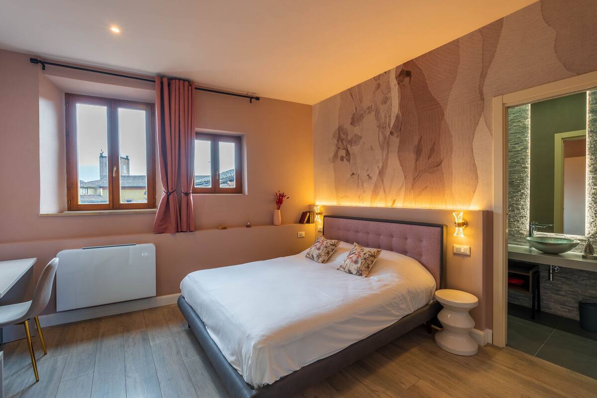 A modern bedroom with a large bed, a desk, and a view of the city.