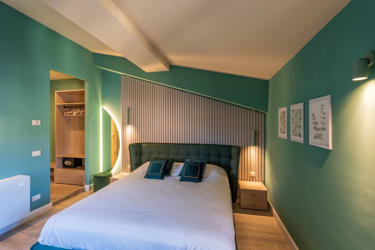 A modern bedroom with a large bed, a walk-in closet, and a wall-mounted light fixture.
