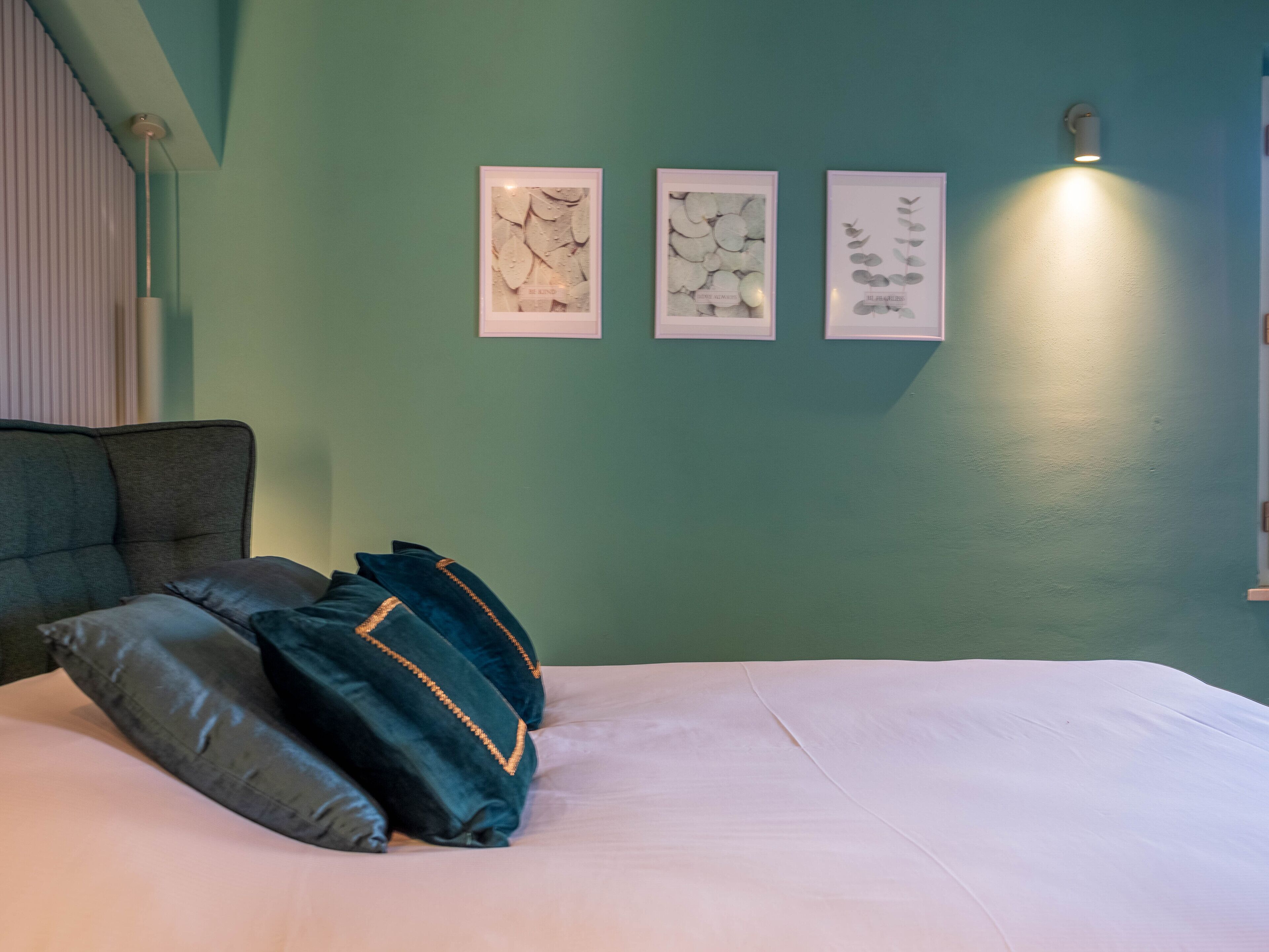 Een slaapkamer met een bed, kussens en drie ingelijste kunstwerken aan de muur.