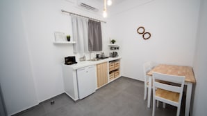 A compact kitchen with white cabinets, a wooden dining table, and a small refrigerator. - Eunoia apartments (Santorini)