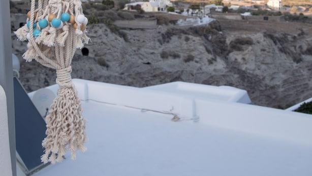 A macrame hanging ornament with a view of the sea and distant buildings. - Eunoia apartments (Santorini)