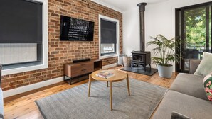 A living room with a brick wall, a fireplace, a TV, and a sofa. - Pretty Prince - Modern 4 Bedroom Home near CBD (Orange)