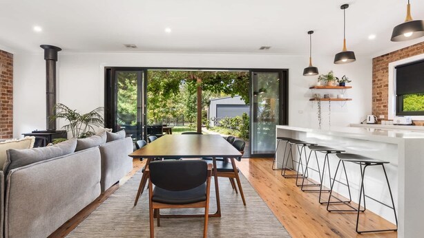 A modern kitchen with a central island, bar stools, and a dining area with a table and chairs. - Pretty Prince - Modern 4 Bedroom Home near CBD (Orange)