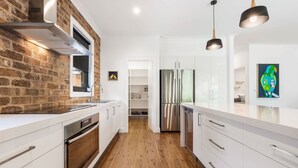 A modern kitchen with a brick wall, stainless steel appliances, wooden flooring, and white cabinetry. - Pretty Prince - Modern 4 Bedroom Home near CBD (Orange)