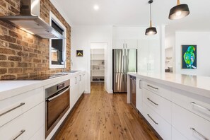 A modern kitchen with a brick wall, stainless steel appliances, wooden flooring, and white cabinetry.