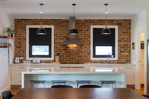 A modern kitchen with brick walls, pendant lights, a central island with bar stools, and a window above the sink.