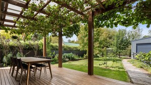A wooden deck with a pergola, a table with chairs, and a well-maintained garden. - Pretty Prince - Modern 4 Bedroom Home near CBD (Orange)