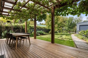 A wooden deck with a pergola, a table with chairs, and a well-maintained garden.