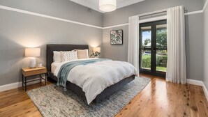 A bedroom with a bed, bedside lamps, a window with curtains, and a view of the outdoors. - Pretty Prince - Modern 4 Bedroom Home near CBD (Orange)