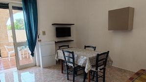 A dining area with a table and chairs, a television on a shelf, and a sliding glass door leading to an outdoor area. - Apartment with Veranda 200 meters from the waterfront (TORRE SAN GIOVANNI)