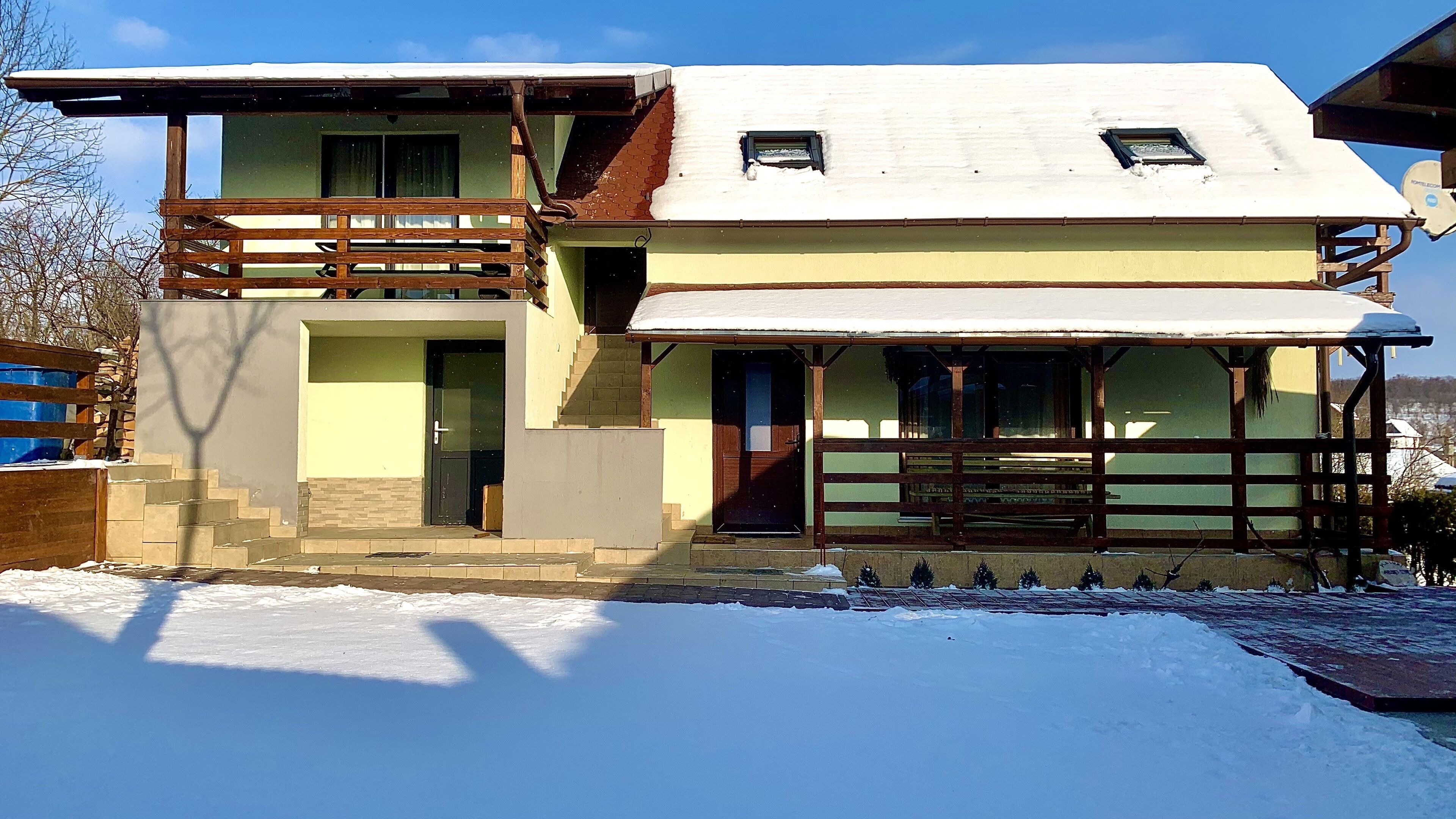 A two-story house with a balcony, a front porch, and a snow-covered roof.