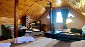 A cozy attic bedroom with a sloped ceiling, a brick fireplace, a television, and a comfortable seating area with a sofa and a chair.