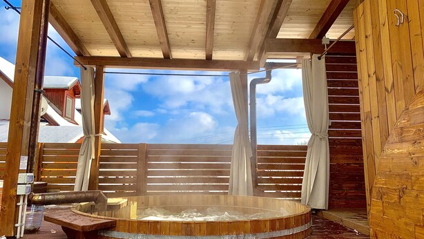 A wooden sauna with a bench, a hot tub, and a view of the sky.