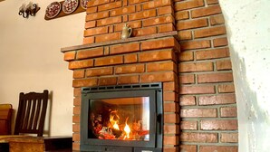 A brick fireplace with a visible fire, wooden beams on the ceiling, and a tiled floor.