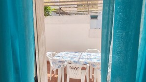 Un patio al aire libre con una mesa y sillas, un muro blanco y una estructura de techo de paja.