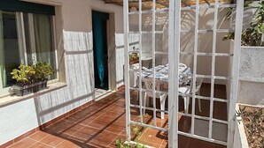 Un porche cubierto con una mesa, sillas, una ventana con cortinas y plantas en macetas.