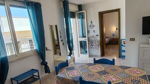 A room with a round table covered with a colorful patchwork tablecloth, blue chairs, a small blue bench, and a door leading to another room. - Apartment with Veranda in Residence (TORRE SAN GIOVANNI)