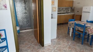 A compact kitchen with wooden cabinets, a white refrigerator, and a dining area with blue chairs and a patterned tablecloth. - Apartment with Veranda in Residence (TORRE SAN GIOVANNI)
