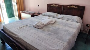 A neatly made bed with a white comforter and two pillows, a wooden headboard with decorative carvings, a bedside table with a lamp, and a window with curtains. - La Palma Residence Two Bedroom Apartment (TORRE SAN GIOVANNI)