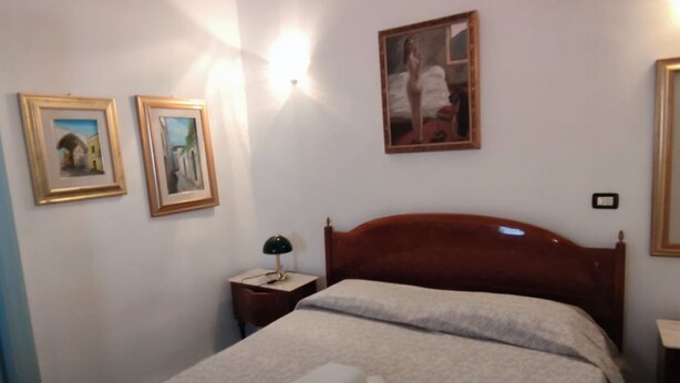 A neatly made bed with white linens and a folded towel, a wooden headboard, a nightstand with a lamp, and two framed pictures on the wall. - RICHARD COMFORT - STUDIO APARTMENT WITH PATIO (TORRE SAN GIOVANNI)