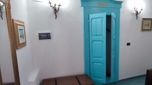 Un couloir avec une porte turquoise portant l’inscription « 1943 », un tableau encadré accroché au mur et une commode marron.
