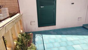 Un petit espace extérieur doté d’une porte verte, d’un portail en métal et d’un sol carrelé.