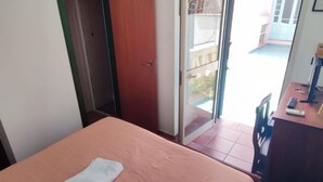 Une chambre comprenant un lit, un bureau et une porte-fenêtre coulissante donnant sur un espace extérieur.