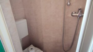 Une petite salle de bain avec des toilettes, une douche et un rouleau de papier toilette posé sur le sol.