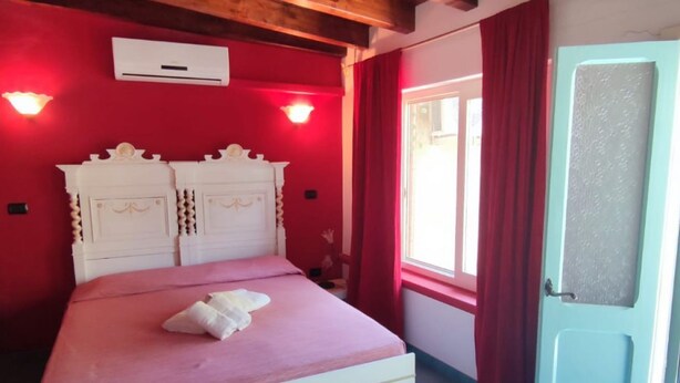Une pièce avec un lit, des murs rouges, une fenêtre avec des rideaux rouges et une porte en verre dépoli.