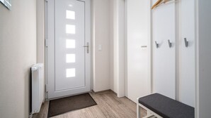 Un pasillo con una puerta blanca, un radiador, un banco y un armario con espacio para colgar ropa.