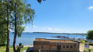 Un edificio de madera con terraza, con vista a un lago con barcos y una orilla distante.