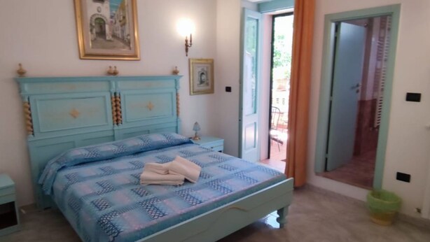 Une chambre à coucher comprenant un lit, une table de chevet, une commode et une porte donnant sur un espace extérieur.