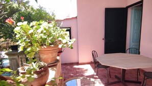 Une terrasse avec une table et des chaises, entourée de plantes en pot et donnant sur une porte.