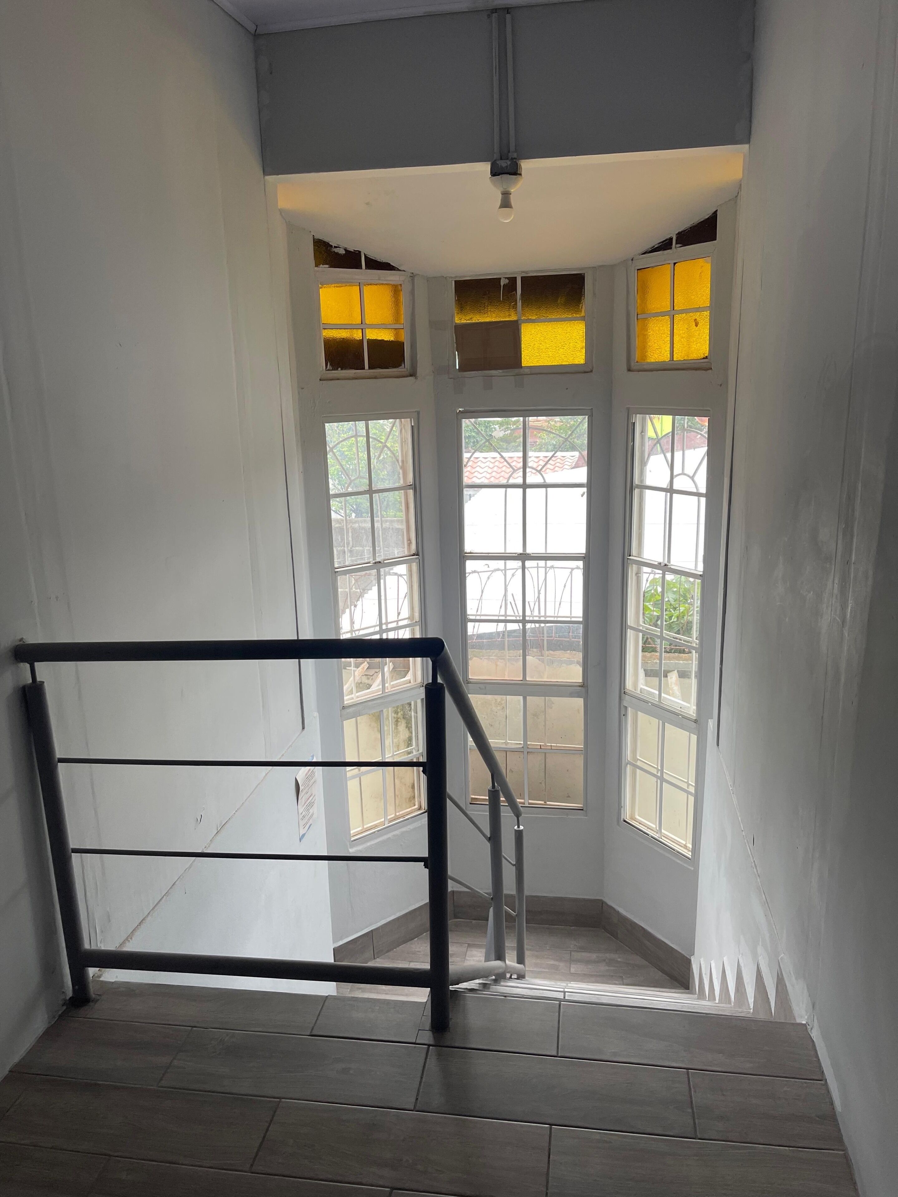 A staircase with a metal handrail leading to a landing with a door and windows.