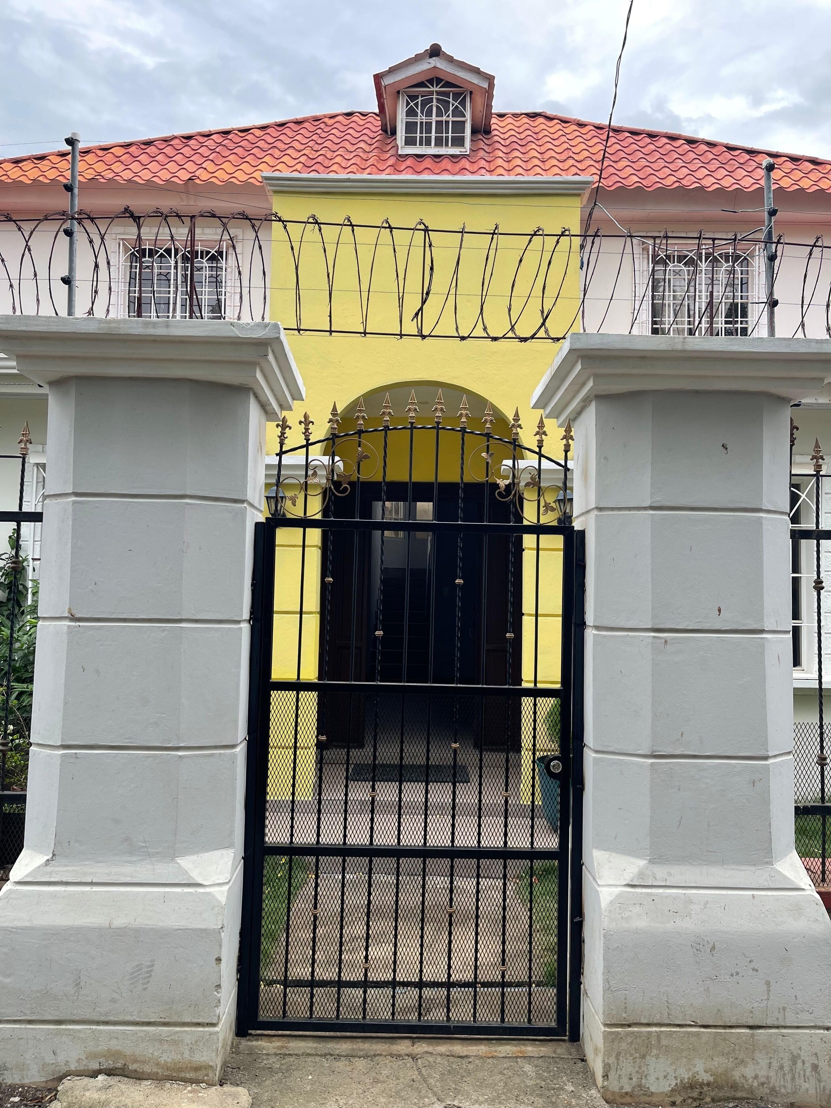 A gated entrance with a yellow facade and a red-tiled roof.